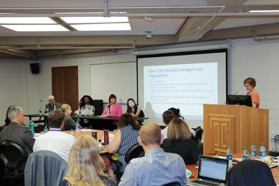 A room of people sits and listens to a presentation and panel.