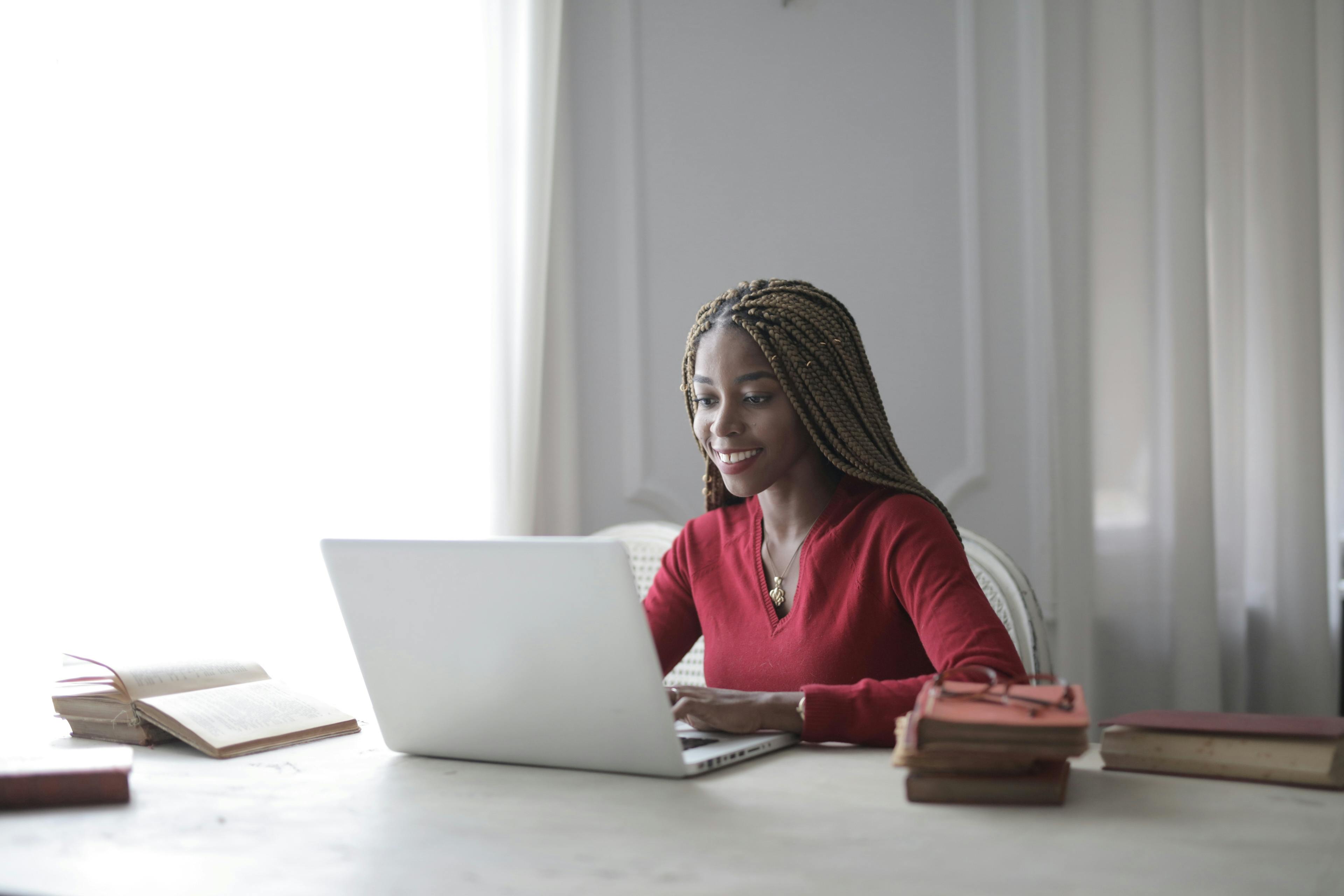 A woman smiles while looking at a lap top computer with her finger on the mousepad.