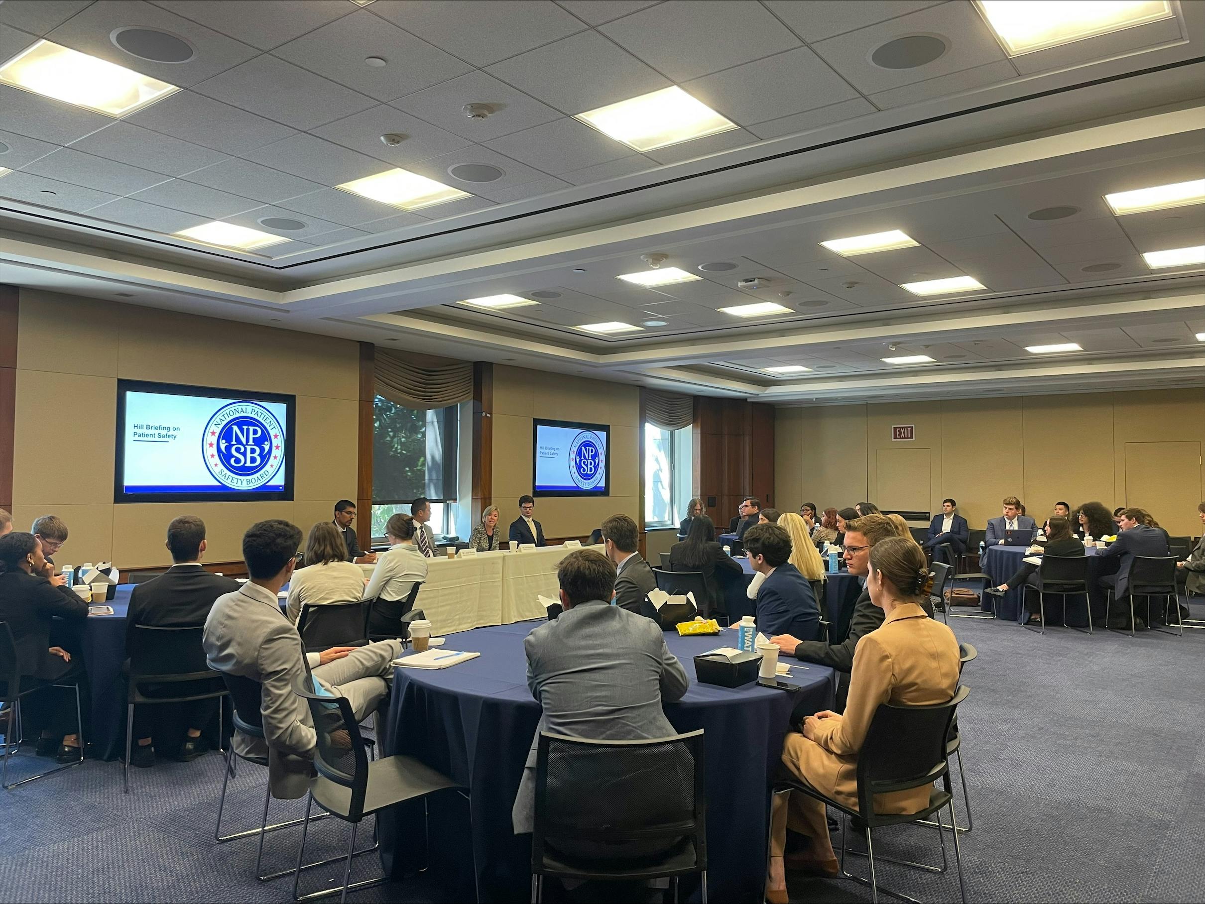 A room of people sitting at round tables watching a presentation.